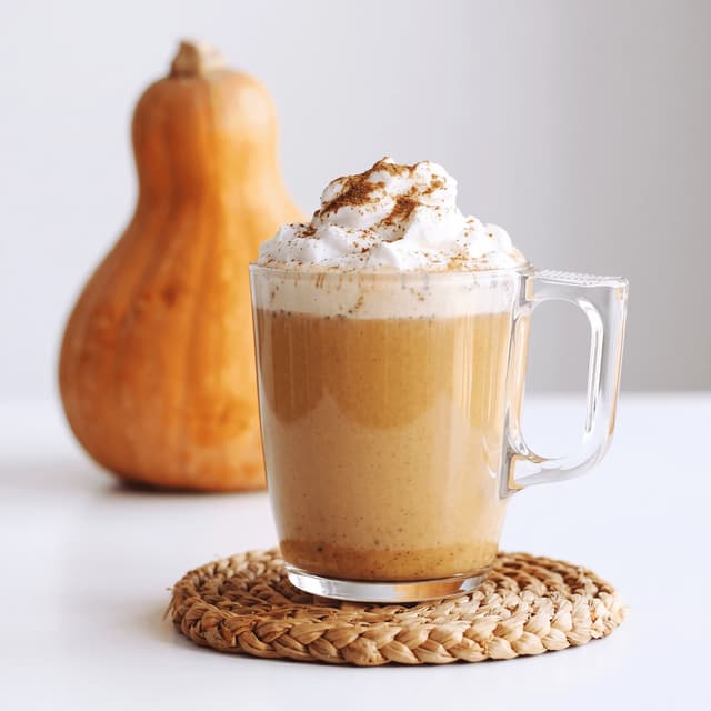 Pumpkin spice latte with whipped cream on a white table — seasonal café drink photography
