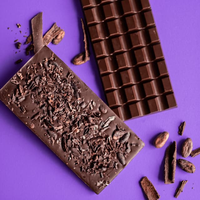 Dark chocolate bars, cocoa nibs and cocoa beans on violet — retail poster food photography