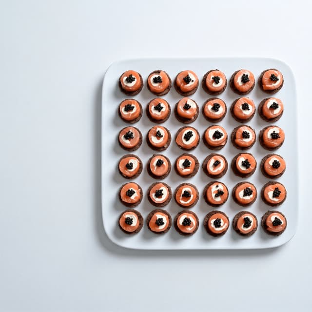 Smoked salmon canapés with caviar on a white platter — catering promo poster photography