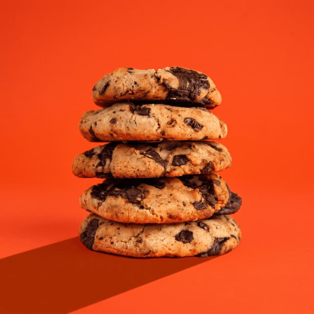 Stacked chocolate chunk cookies on tangerine orange — price promo poster food photography