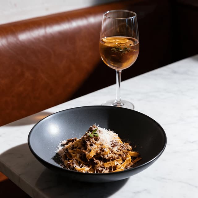 Tagliatelle ragù beside an aperitivo cocktail on white marble — food and drink pairing photography