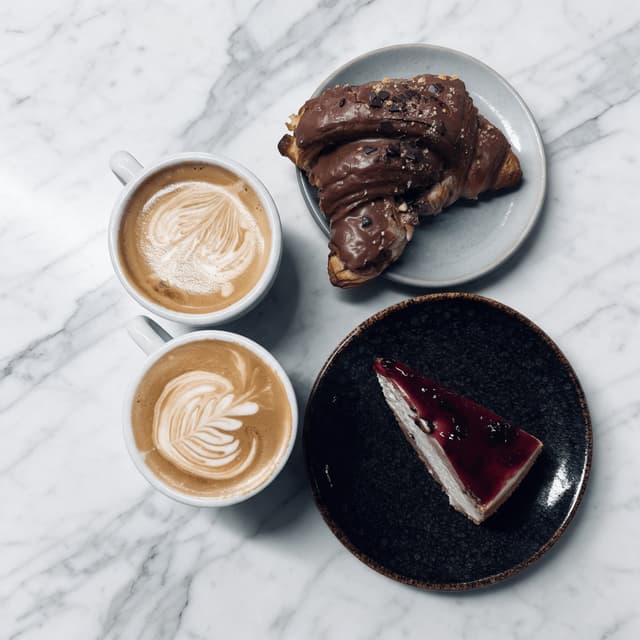 Cappuccinos, chocolate croissant and cheesecake on white marble — hotel café food photography