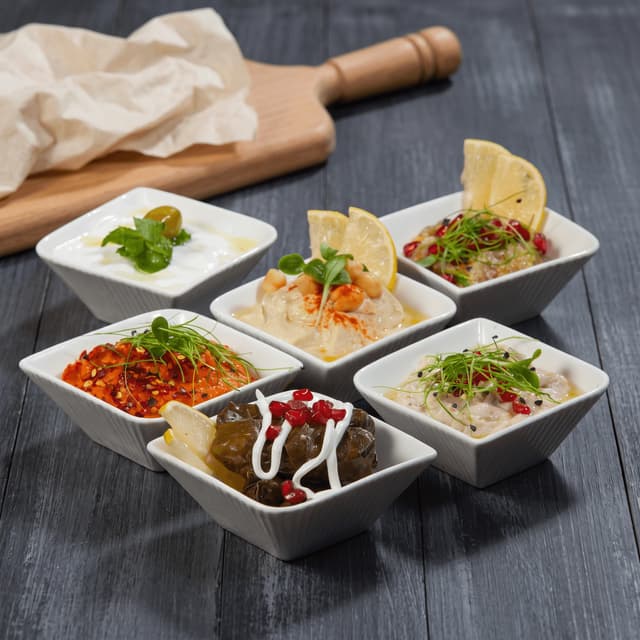Hummus, muhammara and dolma in white bowls on charcoal wood — sharing banner food photography