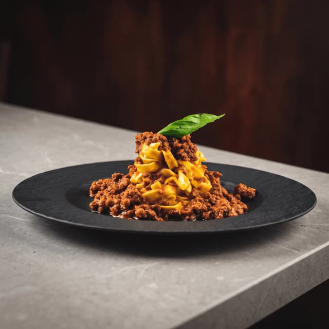 Tagliatelle with beef ragù on a black plate — website hero banner food photography