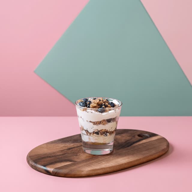 Blueberry yogurt parfait in a glass on pink — cafe brand banner food photography
