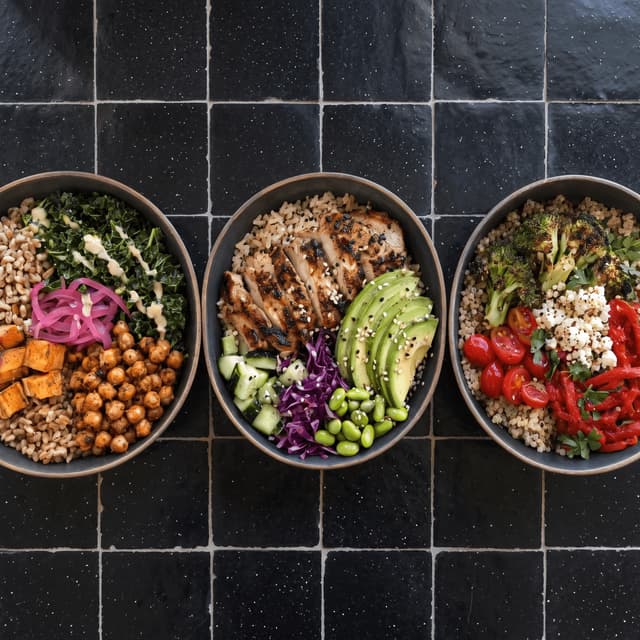 Three matching grain bowls on black tile from above — brand guide food photography