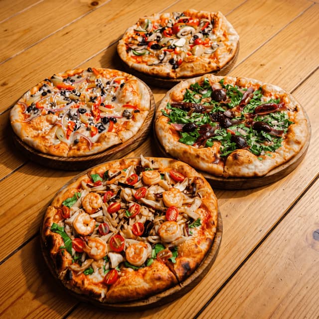 Four pizzas on wooden boards on a pine table — restaurant group menu photography
