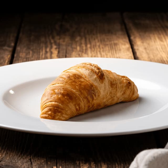 Golden butter croissant on a white plate and dark wood — bakery-café chain food photography
