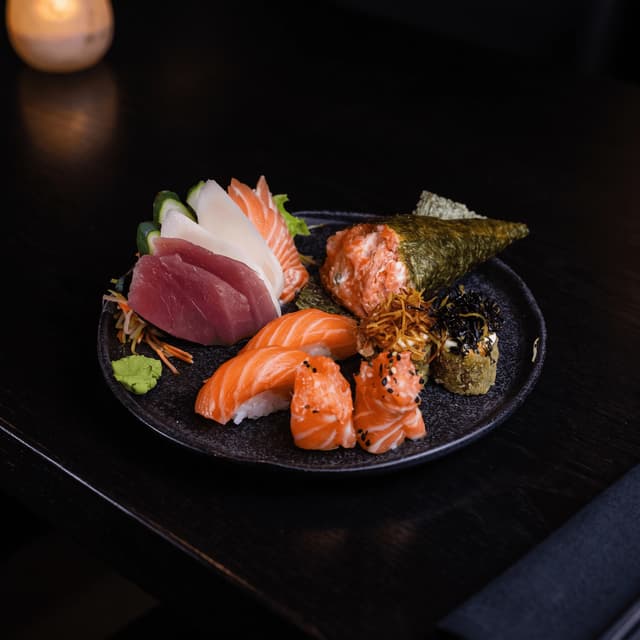 Salmon nigiri, sashimi and a hand roll on a dark plate — sushi restaurant photography