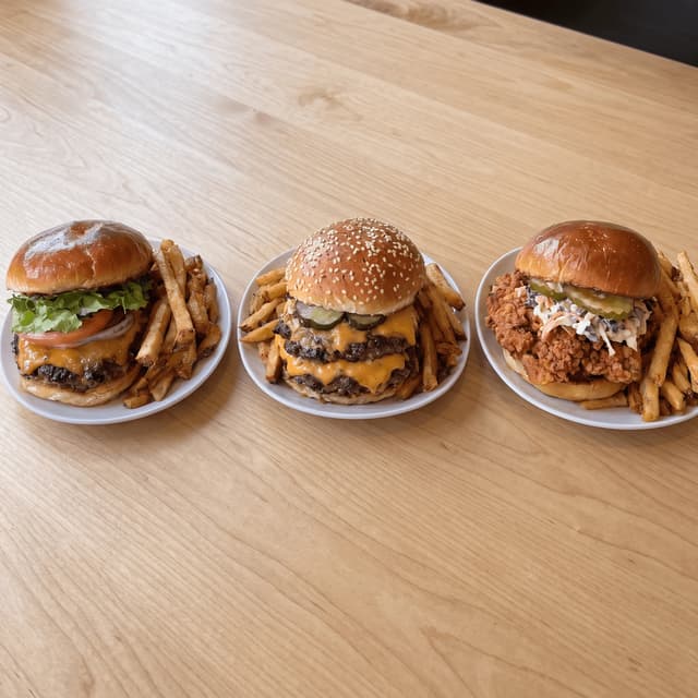 Three burgers with fries on light maple — delivery menu food photography