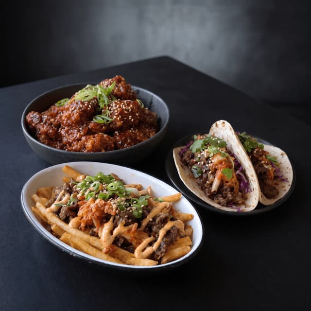 Korean fried chicken, kimchi fries and bulgogi tacos on dark stone — fusion flyer photography