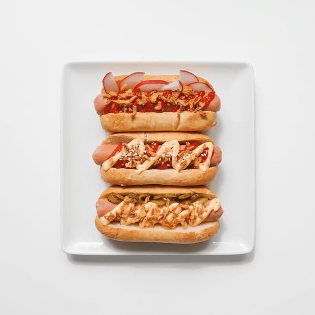 Three loaded hot dogs on a white plate from above — QR-ready flyer food photography