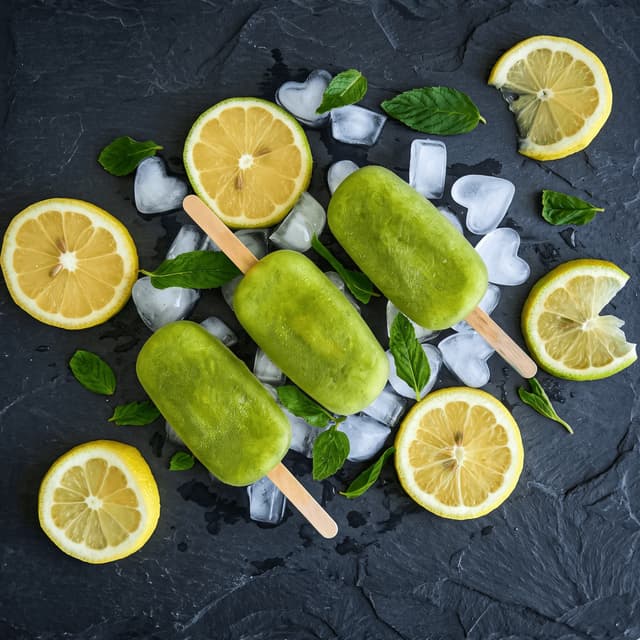 Kiwi-lime ice pops with lemon slices and ice on slate — frozen dessert product photography