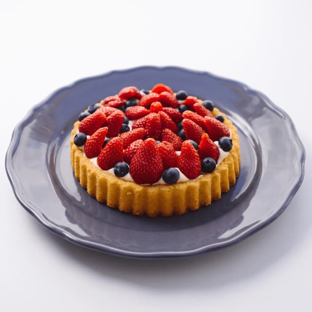 Whole strawberry and blueberry flan tart on a gray scalloped plate — patisserie product photography