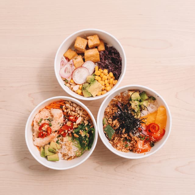 Salmon, shrimp and tofu poke bowls on pale wood from above — fast-casual ad photography