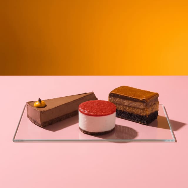 Chocolate tart, berry cheesecake and caramel slice on pink and orange — dessert ad photography