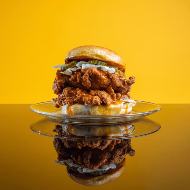 Hot fried chicken sandwich on a glass plate against sunny yellow — restaurant ad photography