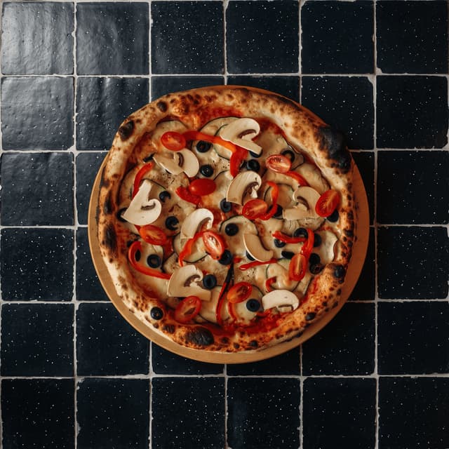 Wood-fired pizza with blistered crust on black tile from above — pizzeria ad photography