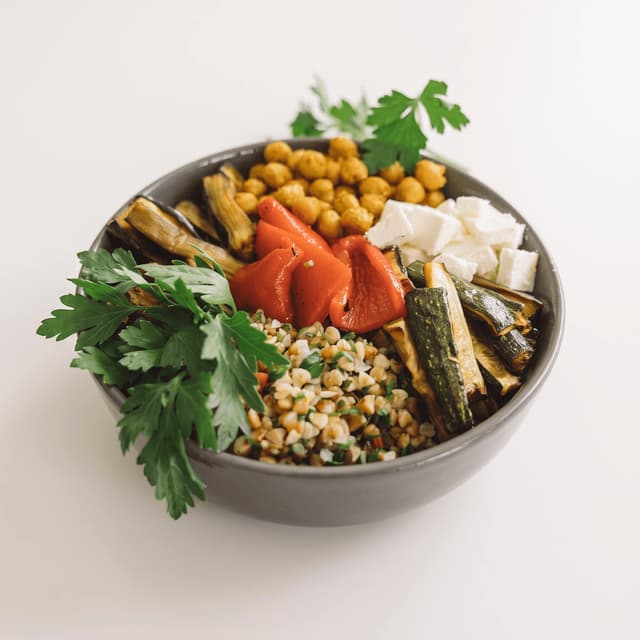 Mediterranean grain bowl with chickpeas, roasted peppers and feta on white — fast-casual ad photography