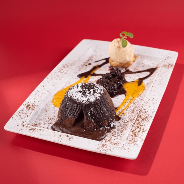 Molten chocolate lava cake with vanilla ice cream on bold red — dessert ad photography