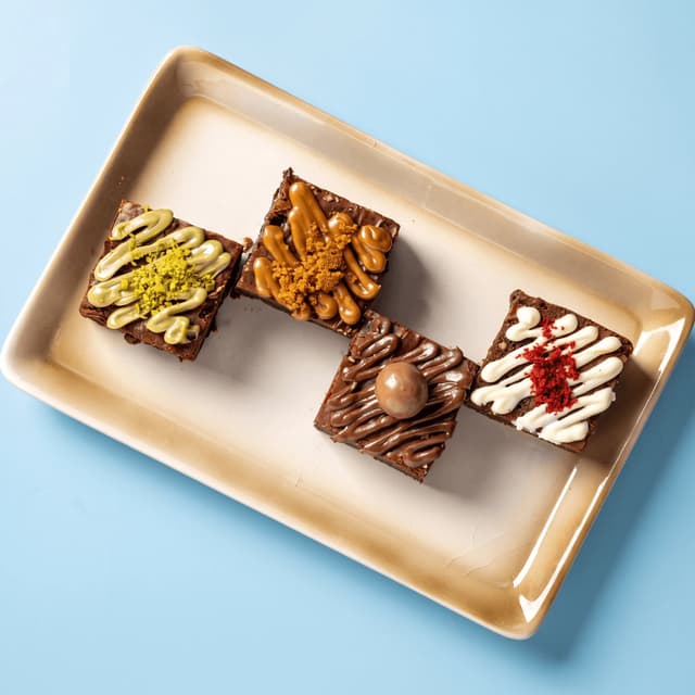 Four topped brownies on a cream platter on pastel blue — dessert flyer food photography