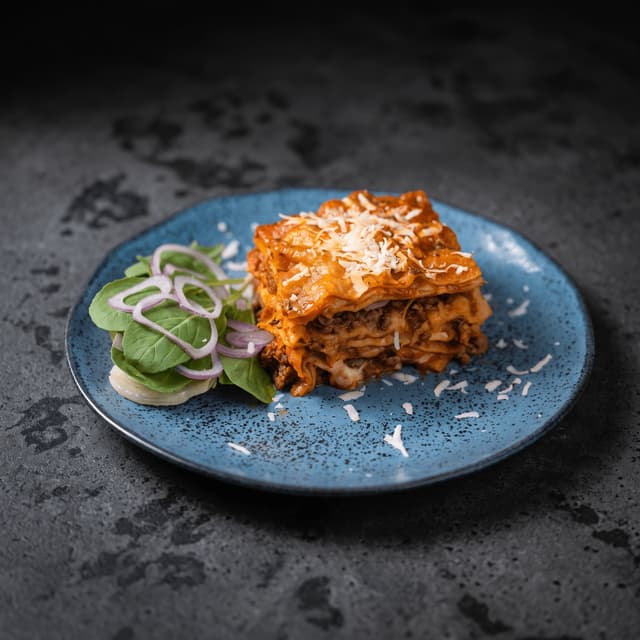 Beef lasagna and side salad on blue stoneware — catering flyer food photography
