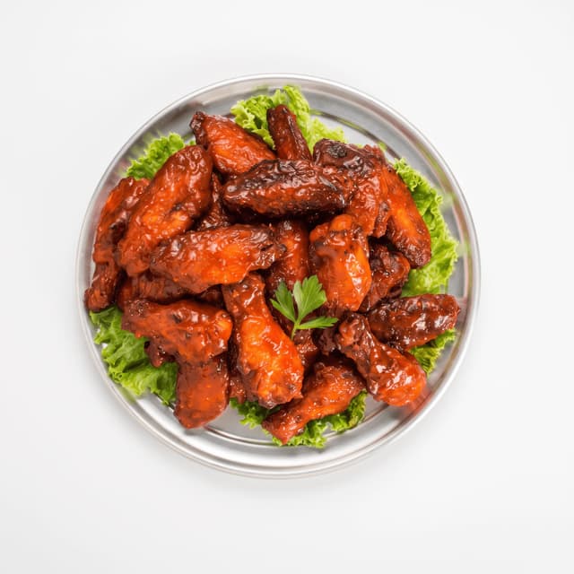Glazed chicken wings on lettuce on a silver plate — delivery flyer food photography