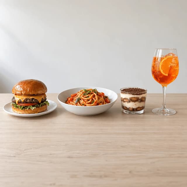 Four restaurant dishes in a row on light wood with clear space above: a burger, pasta, tiramisu and a spritz