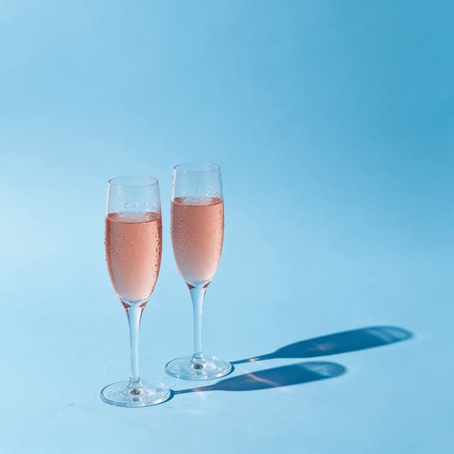 Two flutes of sparkling rosé on a pastel blue set — summer wine photography