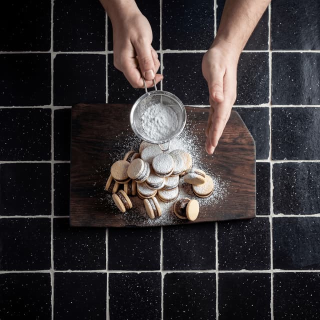 Split alfajor with oozing dulce de leche caramel on dark zellige tile — Argentine filled cookie photography