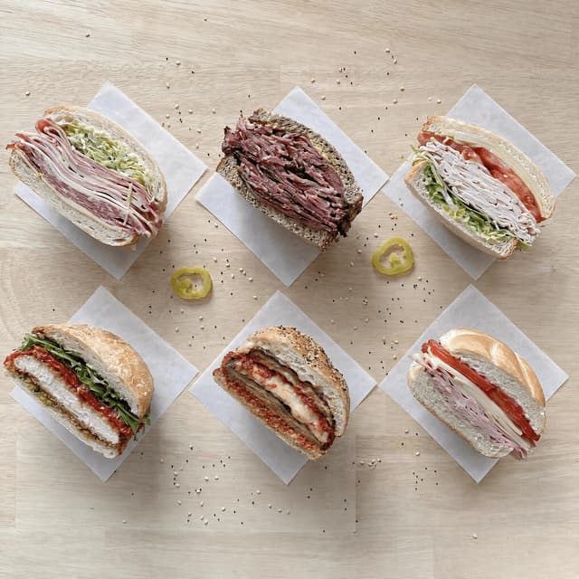 Six different sandwich halves spread evenly across pale blonde wood photographed from directly above