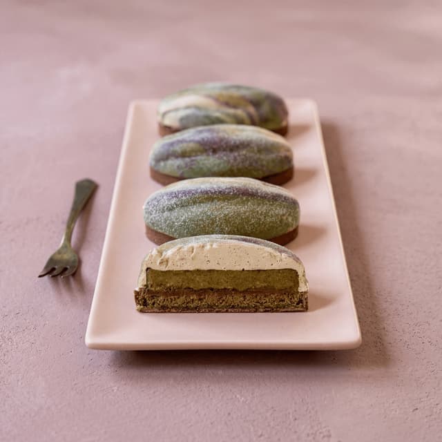 Sculpted pistachio-shell trompe-l'oeil tart with airbrushed green-and-purple glaze on white ceramic — luxury French patisserie photography
