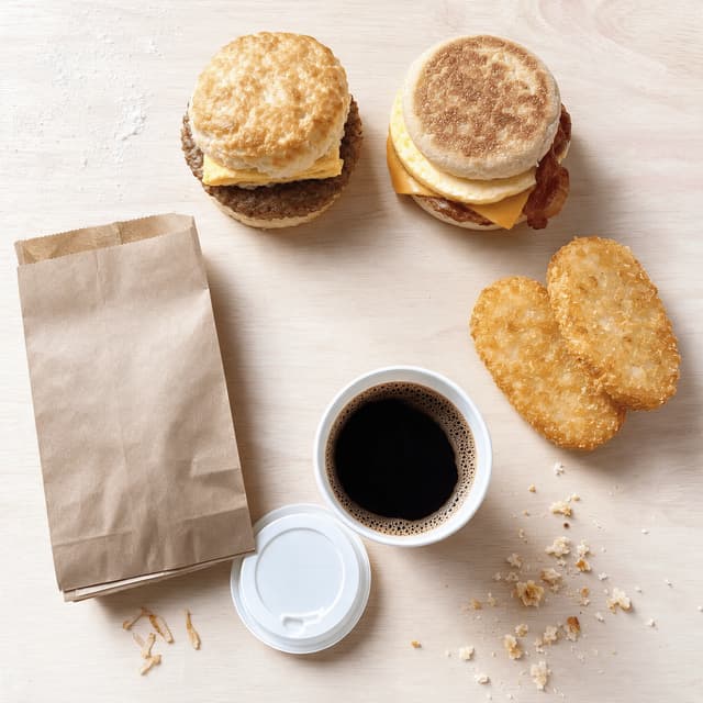Top down breakfast spread with a biscuit sandwich a muffin sandwich hash browns and a coffee cup