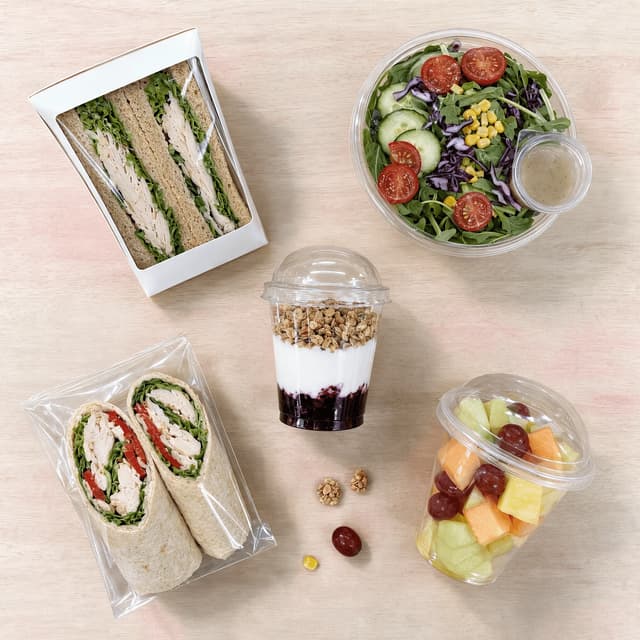 Overhead spread of five packaged fresh items sandwich wedge salad bowl parfait wrap and fruit cup