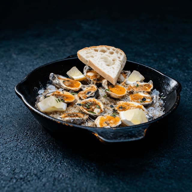 New orleans chargrilled oysters cast iron skillet garlic butter blackened shell rims french bread — chargrilled oysters hero photography