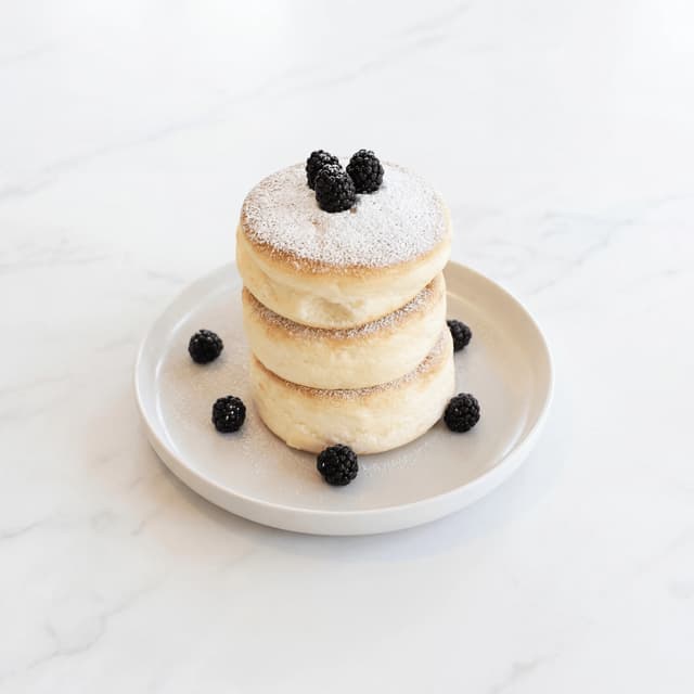 Japońska trzęsąca się wieża pancakes soufflé z cukrem pudrem i jeżynami — viralowa fotografia brunchu z kawiarni