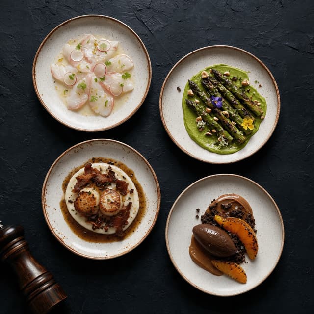 Four different plated tasting menu courses shot from directly above on a dark textured plaster surface