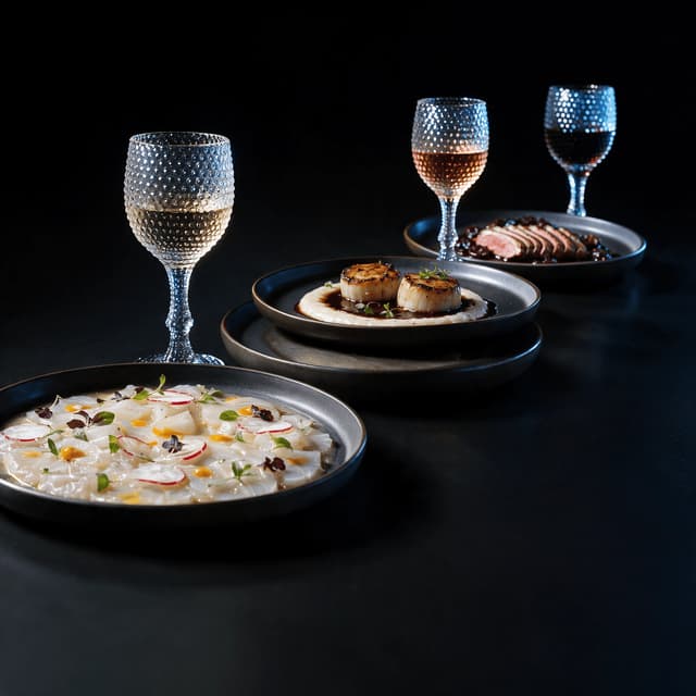 Three plated courses in sequence with paired wine glasses of white, rose and red on a jet black surface