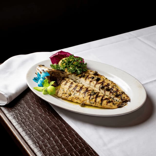 Whole grilled branzino charred lemon herbs plate — coastal seafood hero photography