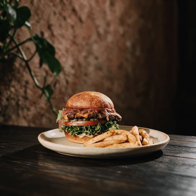 Eén bistro-cheeseburger met gesmolten cheddar op een geroosterd briochebroodje naast een stapel goudbruine friet