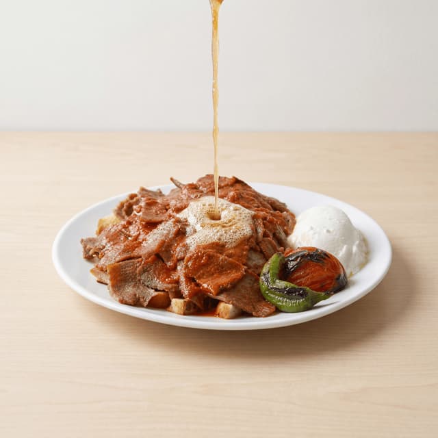 Iskender kebab doner over pide bread tomato sauce yogurt butter pour plate — iskender hero photography
