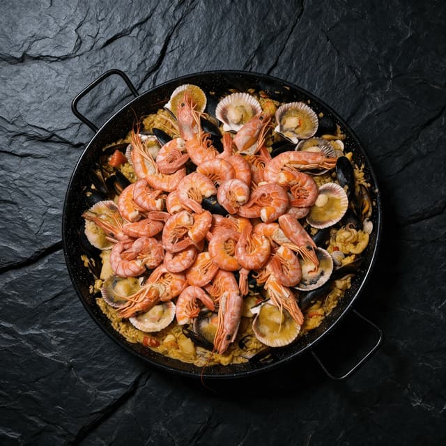 Large seafood paella cooking in a wide steel pan with prawns mussels and lemon wedges at a live station