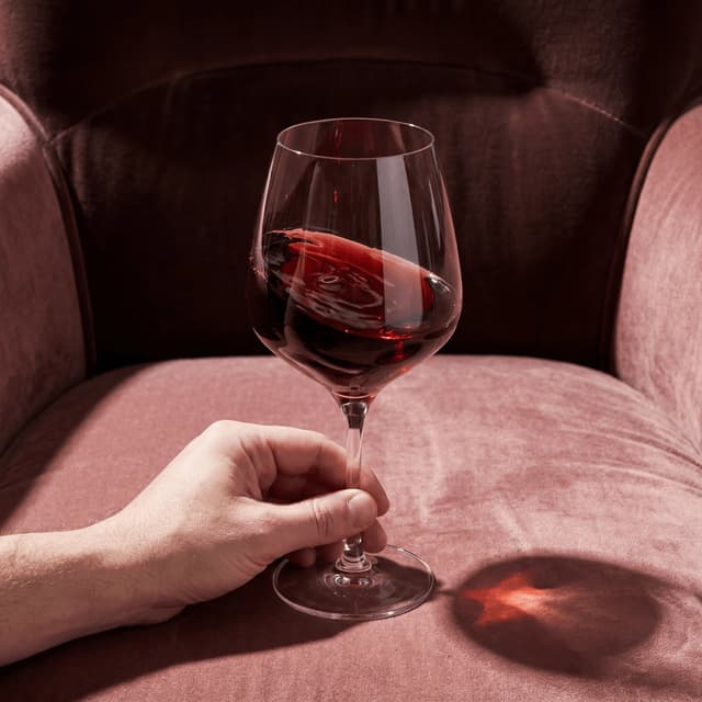 Hand-blown Austrian crystal Burgundy glass with Pinot Noir mid-swirl on walnut counter — fine wine stemware photography