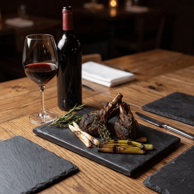 Herb-crusted rack of lamb carved into chops with aged Rioja Gran Reserva glass on graphite slate — Spanish food and wine pairing photography