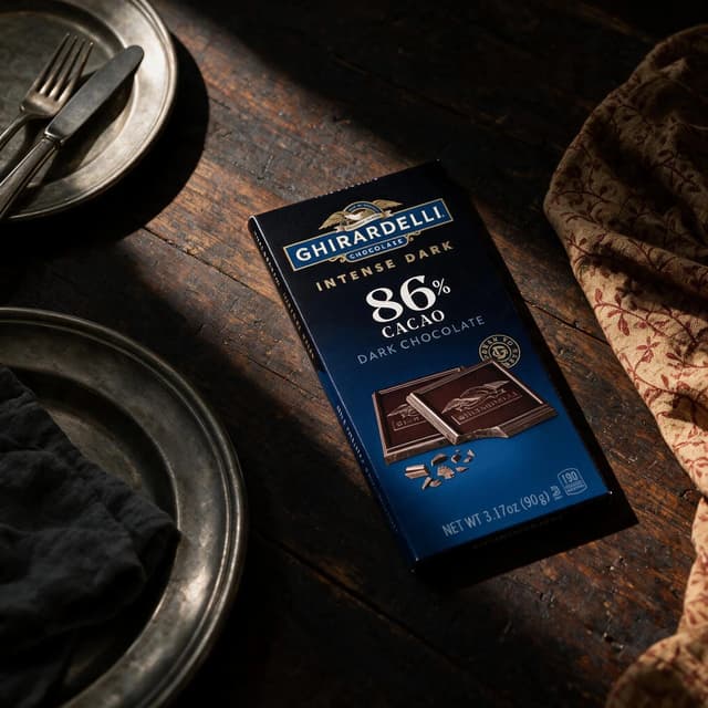 Dark chocolate bar in a moody chiaroscuro still life with pewter plates — premium food photography