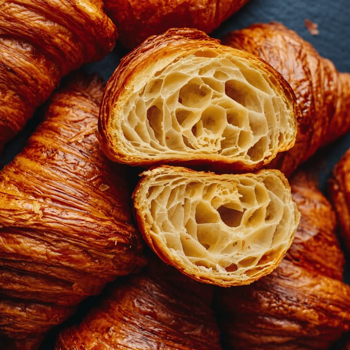 Halved croissant showing flaky layers among golden croissants — bakery poster food photography
