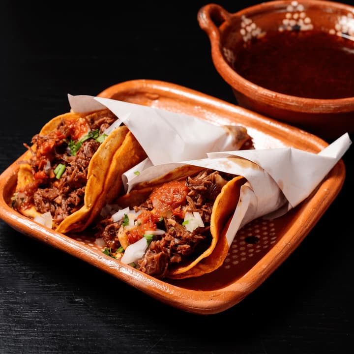 Close view of paper-wrapped birria tacos with consommé — taco truck flyer photography