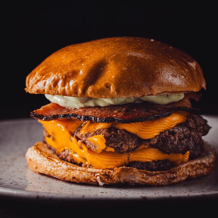Close view of a bacon double cheeseburger with melting cheddar on black — burger ad photography