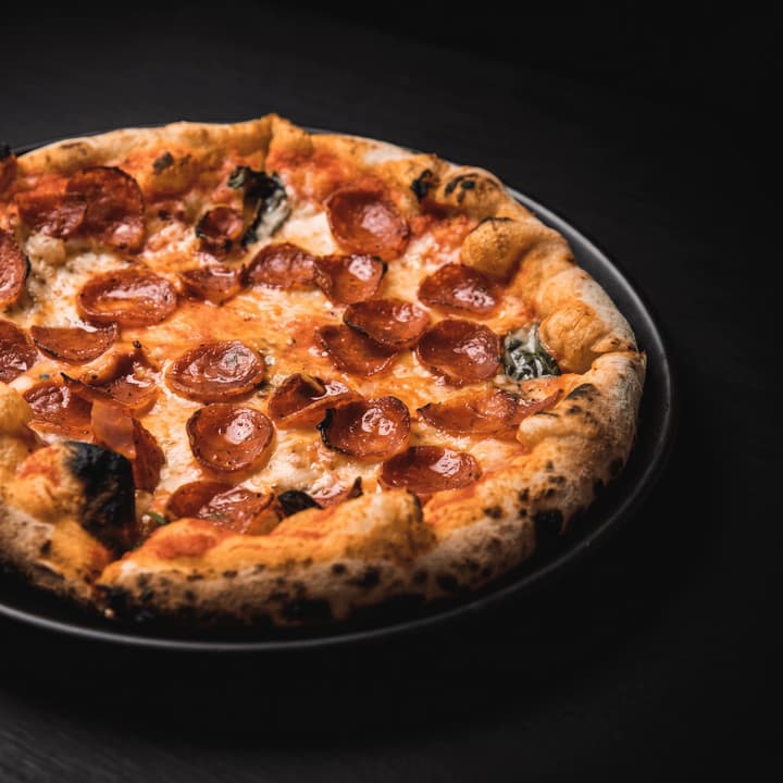 Close view of wood-fired pepperoni pizza on a dark plate — pizzeria flyer photography