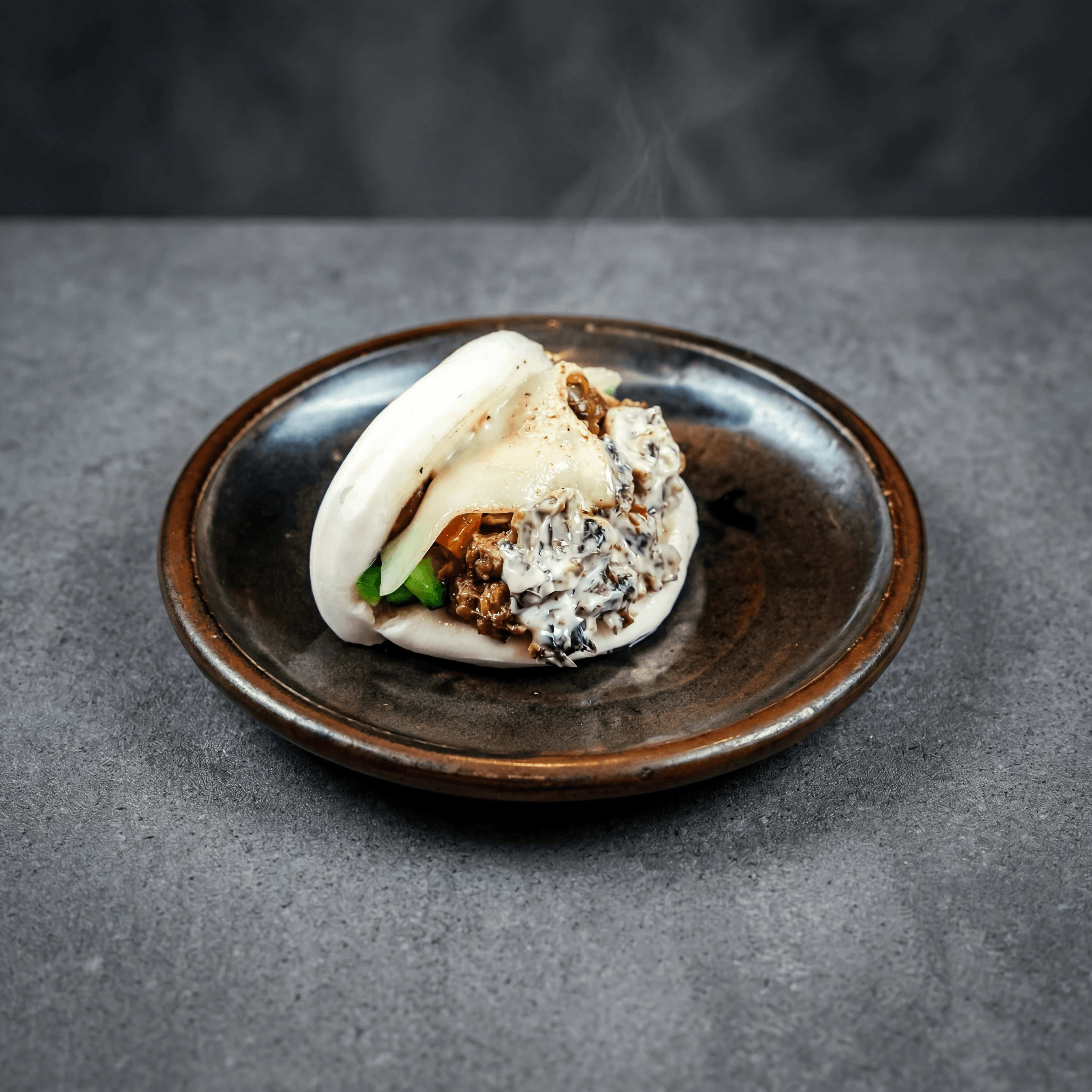 Open-faced pork belly bao bun on dark ceramic plate — ghost kitchen Asian fusion delivery photography